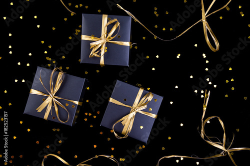Black gift boxes with gold ribbon on shine background. Flat lay.