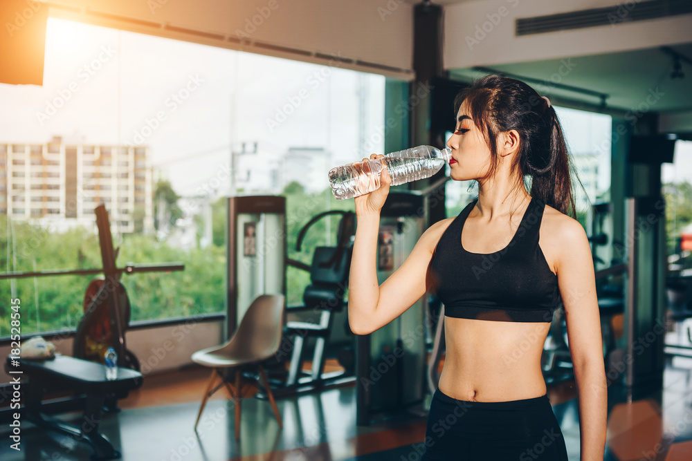 Asian woman exercising in the gym, Young woman workout in fitness for her healthy and office girl lifestyle. She is drinking fresh water.