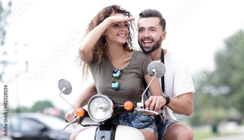 Beautiful young couple is smiling while riding a scooter