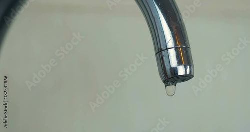 Close-up a droplets of water drip from the aluminum tap in the kitchen at home. 4K.