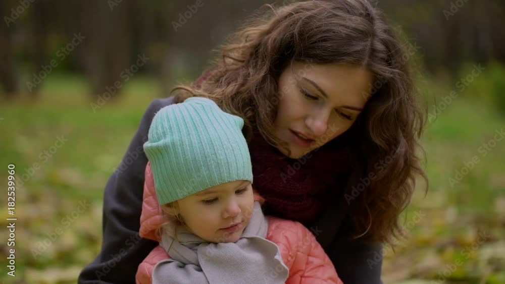 daughter with her mother collecting autumn leaves in the park. In autumn, when yellow leaves around young beautiful mom and girl playing with leaves, laughing and smiling. slow-motion daughter with her mother collecting autumn leaves in the park. In autumn, when yellow leaves around young beautiful mom and girl playing with leaves, laughing and smiling. slow-motion