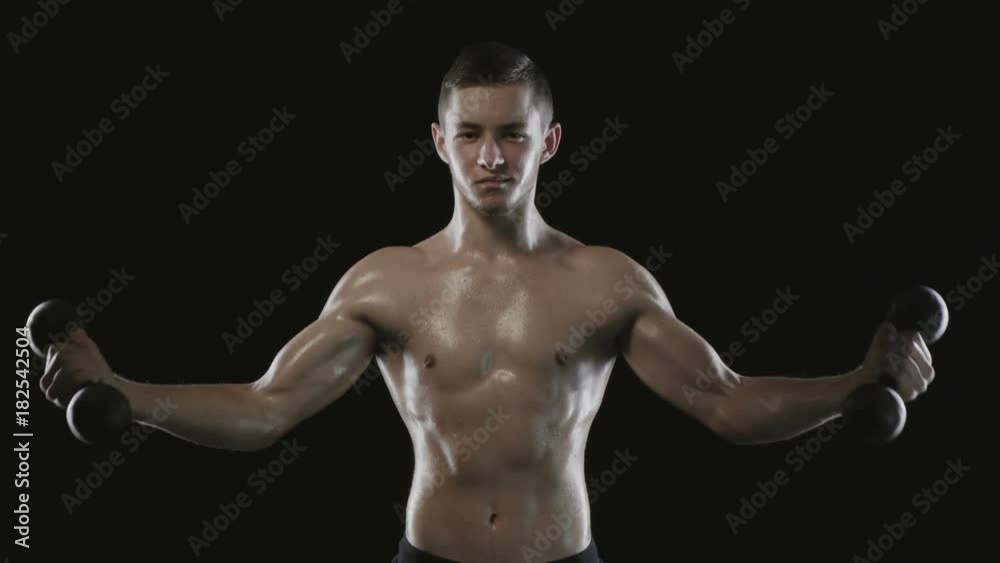 Strong athletic man with muscular torso training with dumbbell over black background Strong athletic man with muscular torso training with dumbbell over black background