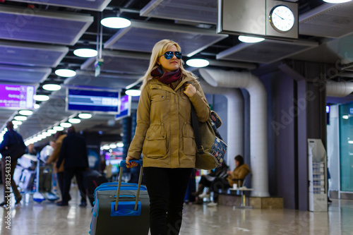 Front view of a traveler woman walking carrying a suitcase in an airport corridor