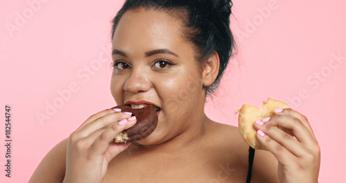 Plus size model in studio shoot happy smiling and eats a donut