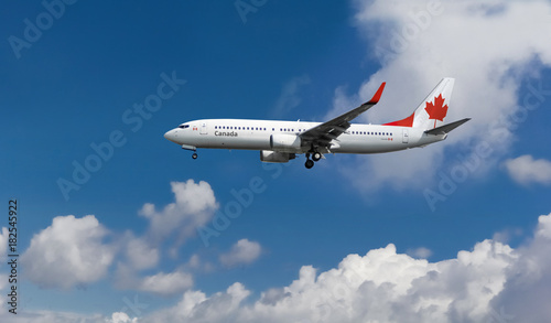 Commercial airplane with Canadian flag on the tail and fuselage landing or taking off from the airport with blue cloudy sky in the background