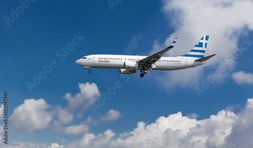 Commercial airplane with flag of Greece on the tail and fuselage landing or taking off from the airport with blue cloudy sky in the background