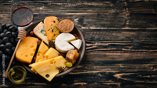 A large assortment of cheeses, brie cheese, gorgonzola, blue cheese, grapes, honey, nuts, red and white wine, on a wooden table. Top view. Free space for text.