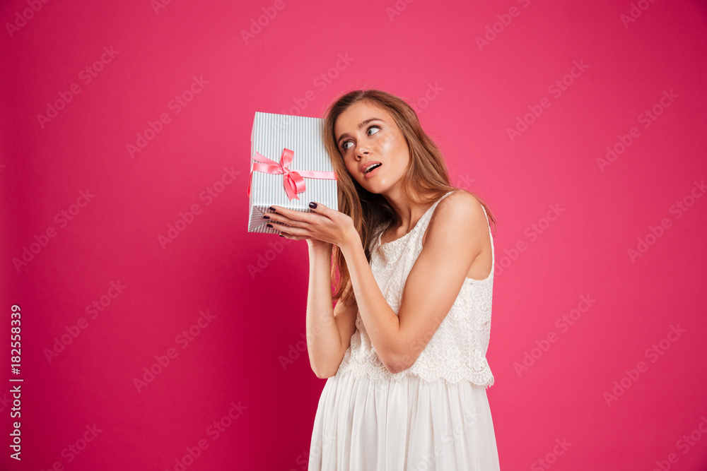 Portrait of a pretty young girl holding gift box at her ear Portrait of a pretty young girl holding gift box at her ear