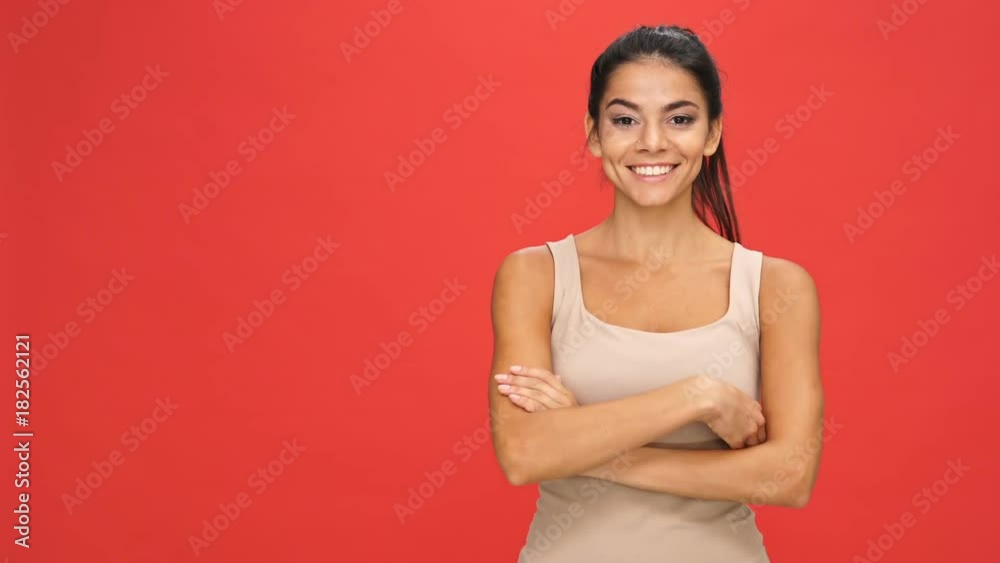 Smiling brunette woman in singlet pointing away and holding crossed arms after that over red background Smiling brunette woman in singlet pointing away and holding crossed arms after that over red background