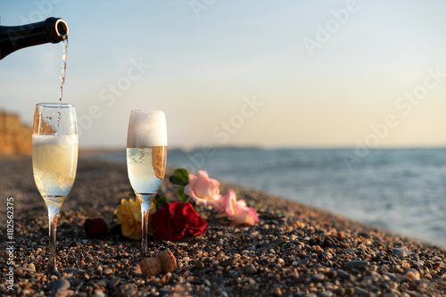 Bottle of champagne, two glasses and rose flowers on the beach. in Greece