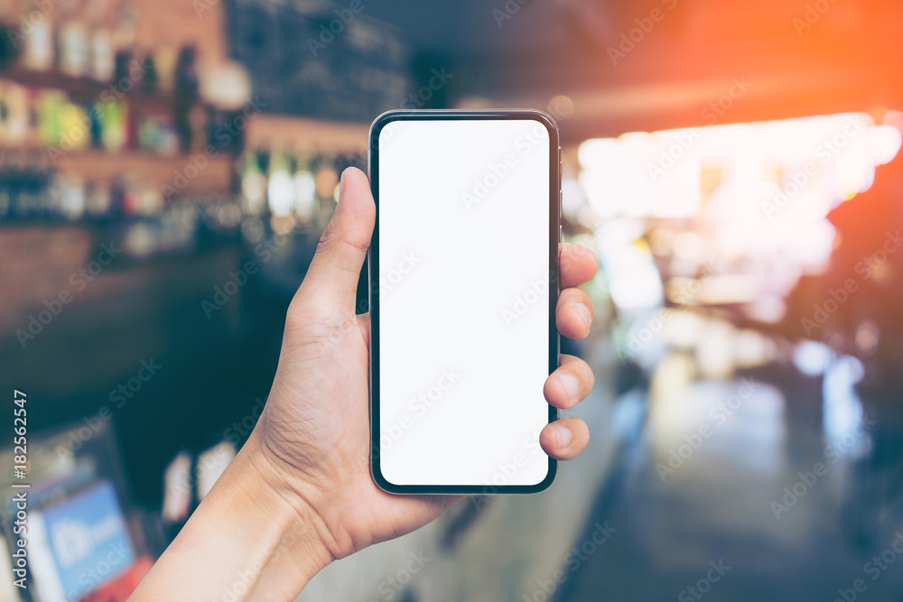 Man's hand shows mobile smartphone with white screen in vertical position, Blurred or Defocus image of Coffee Shop or Cafeteria for use as Background vintage tone. - mockup template and clipping path Man's hand shows mobile smartphone with white screen in vertical position, Blurred or Defocus image of Coffee Shop or Cafeteria for use as Background vintage tone. - mockup template and clipping path