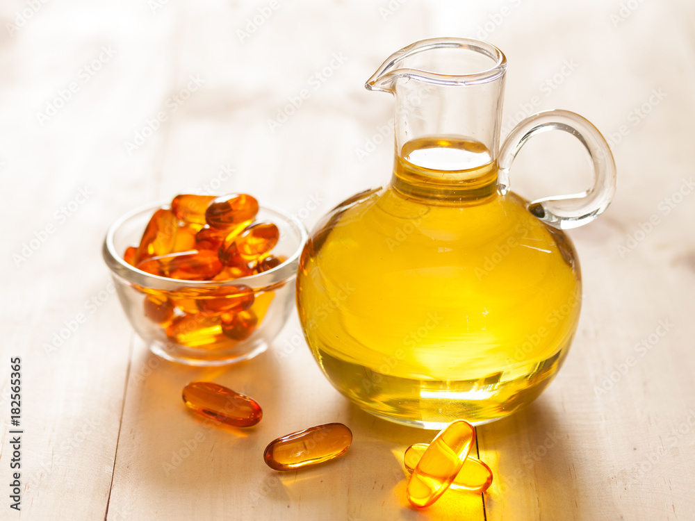 Fish oil in a jug and capsules on wooden texture and table Fish oil in a jug and capsules on wooden texture and table