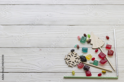 A light wooden Christmas background. A right bottom corner framed with straws, wooden toys and colored candies. Close up. Copy space. Top view