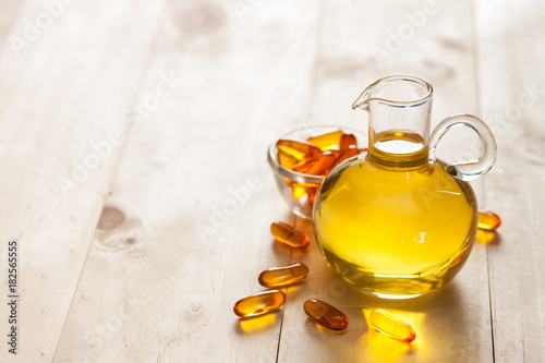 Fish oil in a jug and capsules on wooden texture and table
