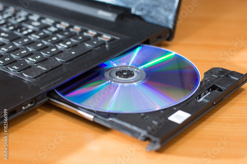 DVD ROM inserted in laptop computer on wooden texture background