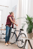handsome cheerful man talking on smartphone and standing with bike at home