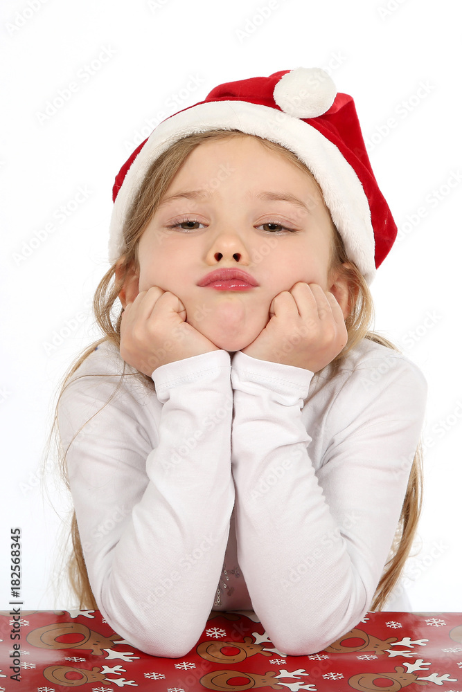 Kleines Mädchen mit Weihnachtsmütze stützt ihr Kinn in den Händen und schmollt Kleines Mädchen mit Weihnachtsmütze stützt ihr Kinn in den Händen und schmollt