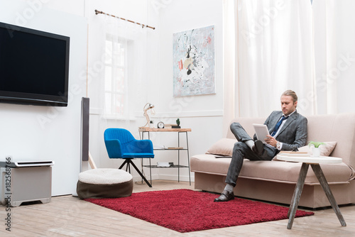 businessman using digital tablet while sitting on sofa at home © LIGHTFIELD STUDIOS