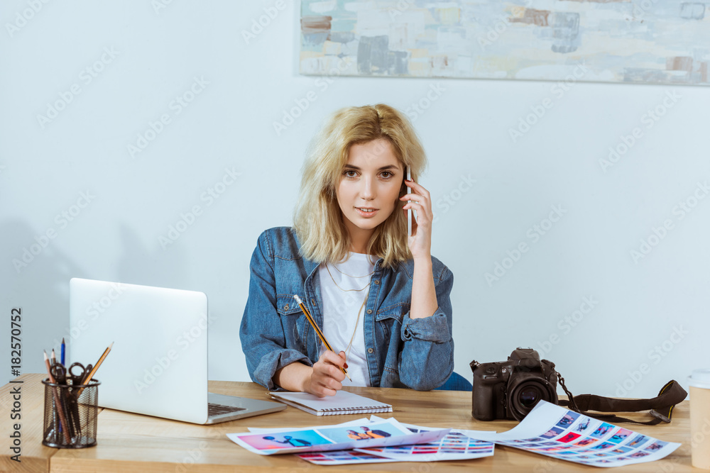 portrait of young photographer talking on smartphone while sitting at workplace in studio