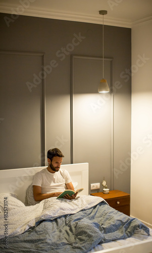 Young man reading book in bed