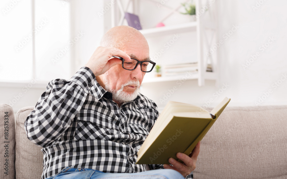 Senior man reading book at home, copy space