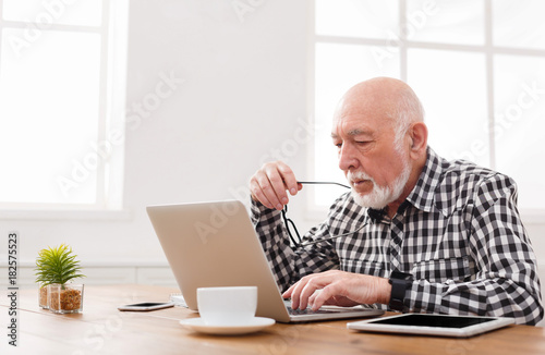 Mature man using laptop and writing in notepad