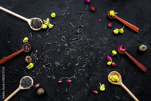 Aromatic tea. Wooden spoons with dried tea leaves, flowers and spices on black background top view copyspace