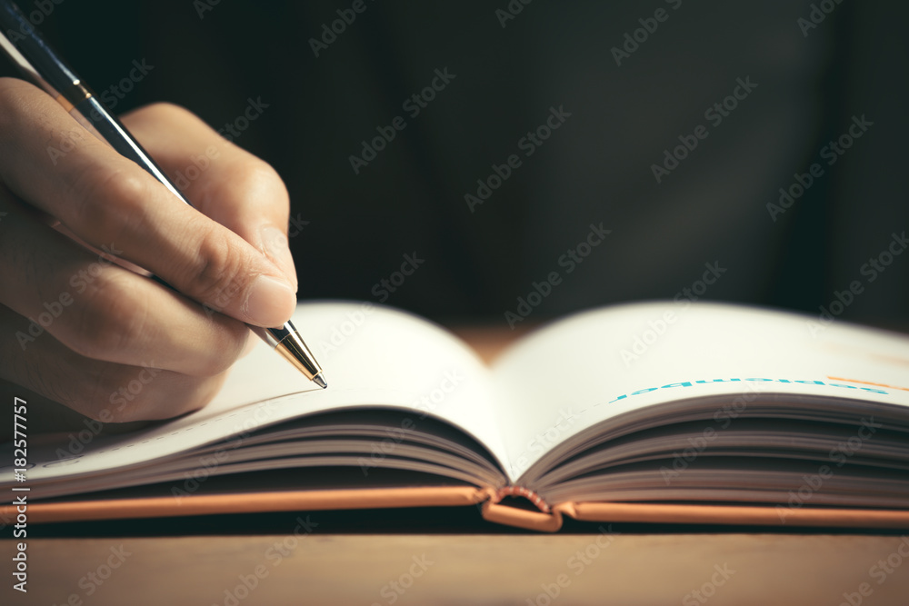 Male hand with pen writing in notebook on desktop Male hand with pen writing in notebook on desktop