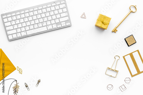 Fashoin in the workplace. Office desk in a trendy gold color. Stationery near keyboard on white background top view copyspace