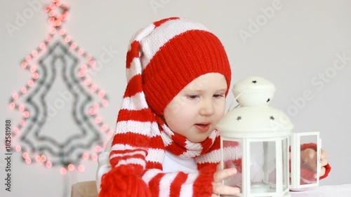 Portrait of a happy funny child in Santa Claus clothes. A pretty girl blows a candle in a lantern and makes a wish on the eve of the new year and Christmas. Magic photo