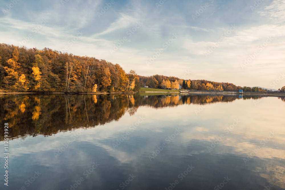 Fototapeta premium Beautiful lake and colorful forest in autumn evening light. Beautiful forest of colorful autumn trees reflecting in calm lake in Duchonka (Slovakia). Fall season. Scenic view of pond in autumn.