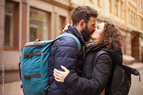 A loving couple of travelers with backpacks kissing outdoors in the old town - Concept of people and love.