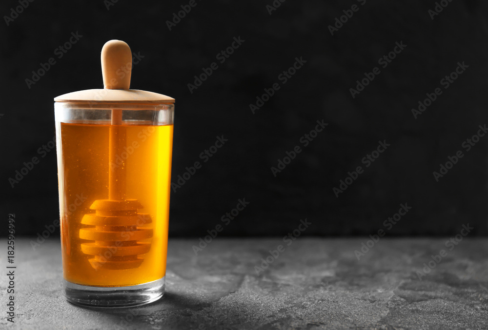 Aromatic honey in glass jar on table against dark background Aromatic honey in glass jar on table against dark background