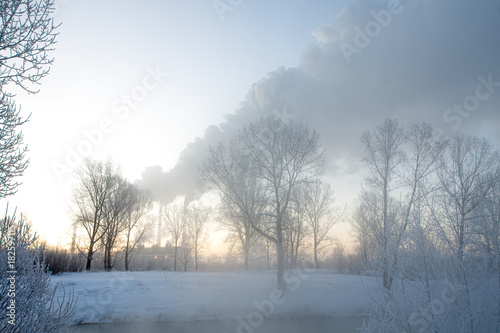 Snowy frozen landscape on sunrise with trees and smoke of factory   © photollurg