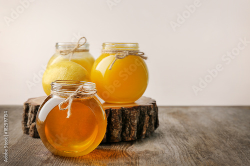 Aromatic honey in glass jars on table against light wall