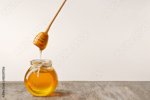 Murais de parede Pouring aromatic honey into jar on table against light wall