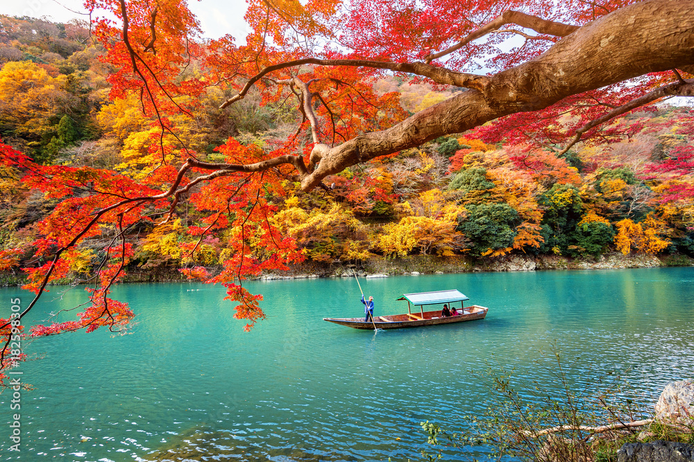 Naklejka premium Boatman punting łódź na rzece. Arashiyama w sezonie jesiennym wzdłuż rzeki w Kyoto, Japonia.