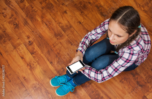 girl in jeans sits on the wooden floor and holding a smartphone. Concept of teenage life and gadgets. Top view with copy space.