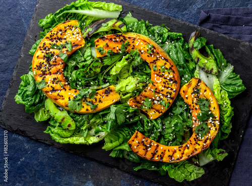 Grilled pumpkin and lettuche salad with white and black sesame and balsamic sauce on slate black board, blue stone background photo