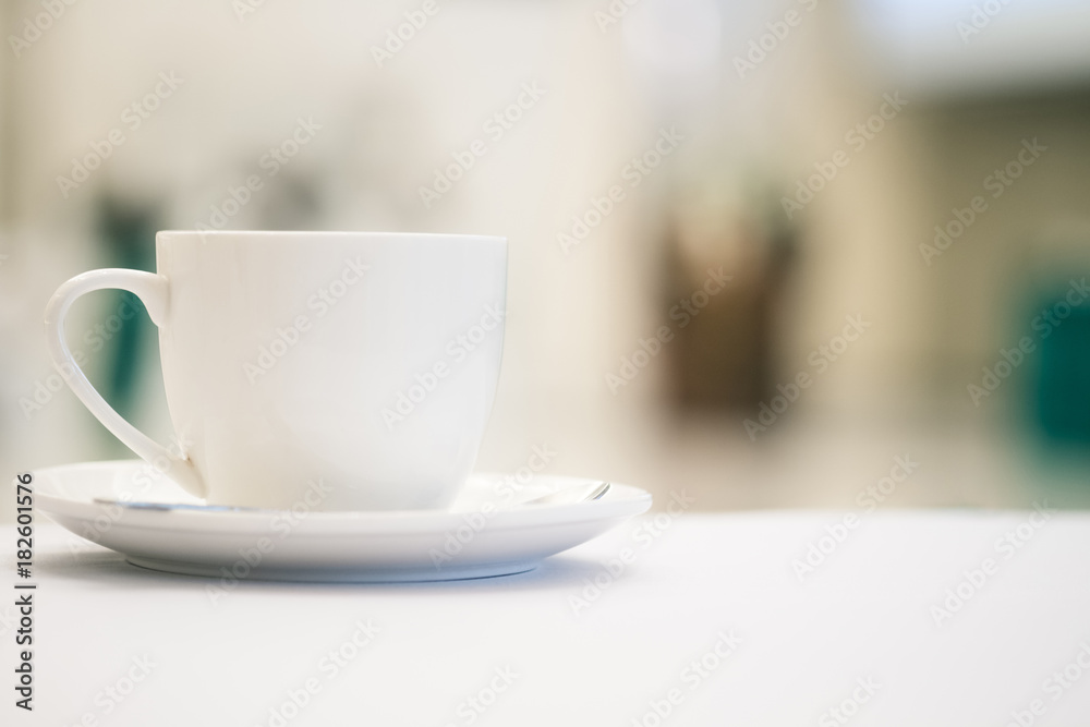 White cup of coffee placed on white table with blurred people have seminar in meeting room background.