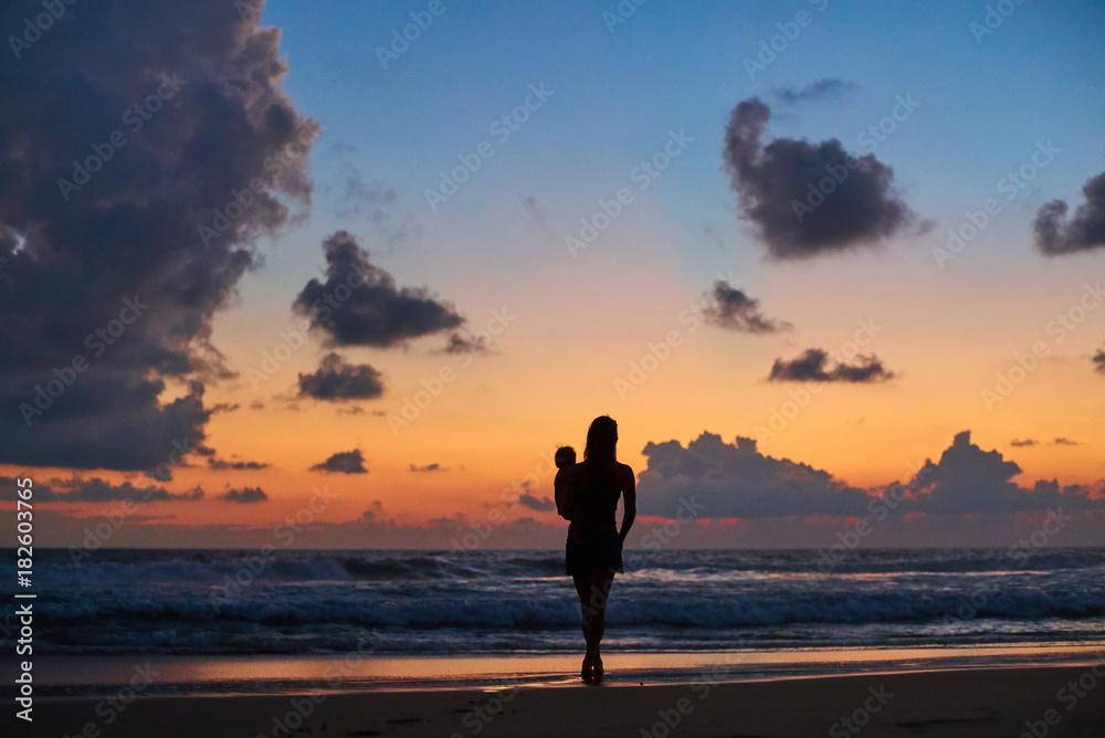 silhouette of mother carrying child in front of beautiful ocean beach sunset