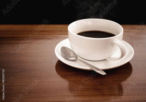 A cup of coffee is placed on a wooden table. The background is black.