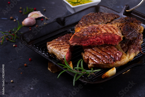 Grilled juisy beef steak in pan with spices on dark stone background