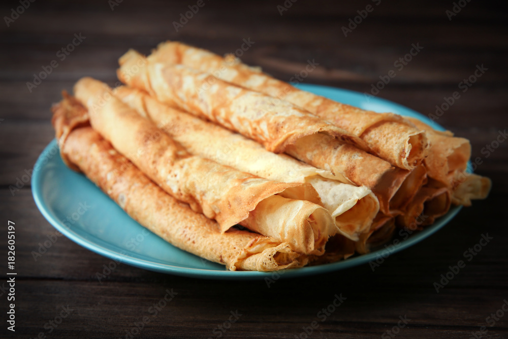 Plate with delicious thin pancakes on table