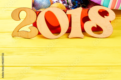Wooden text 2018 and copy space. Number 2018 from wood, box with Christmas balls, space for text on yellow wooden background. Merry Christmas and Happy New Year 2018.