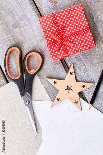 New Year handmade decorations, top view. Scissors, paper, cut out wooden Christmas star, gift box on rustic wooden background.