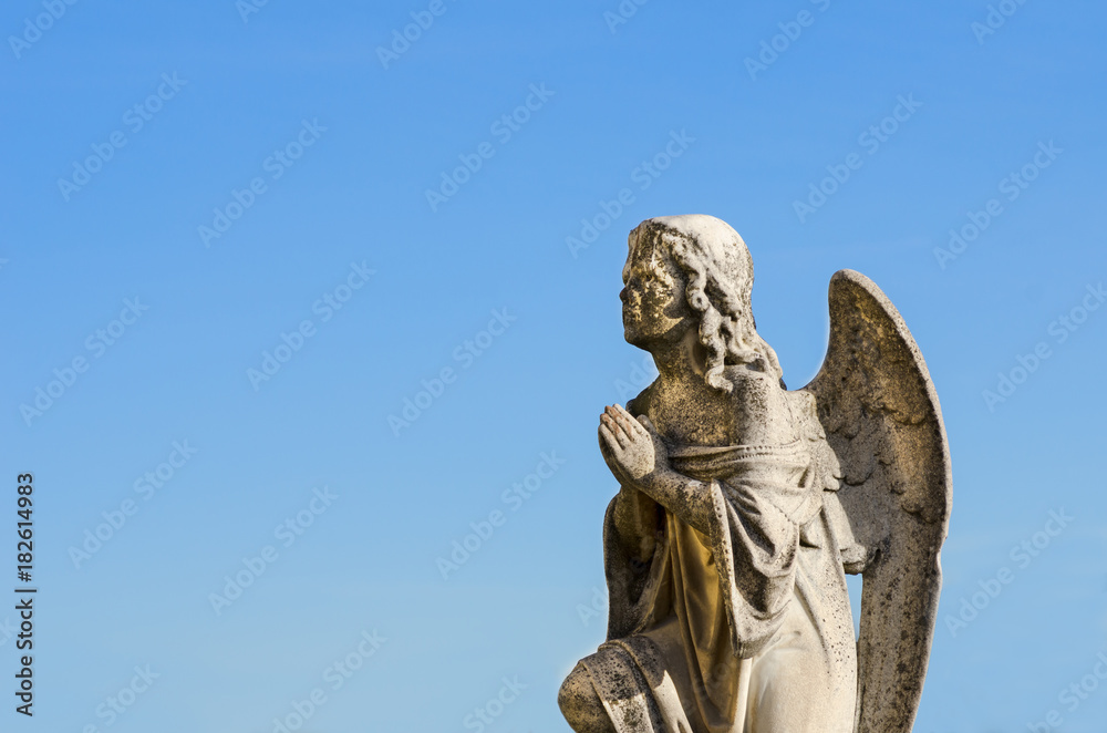 Praying angel pray to God public sculpture on the cemetery with blue sky background