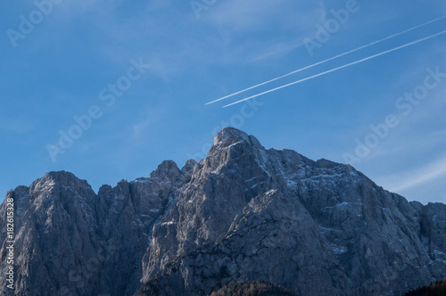 Two airplane contrails parallel to each other over the rugged peaks of the Julian Alps