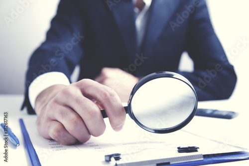 Businessman checking a document with a magnifying glass