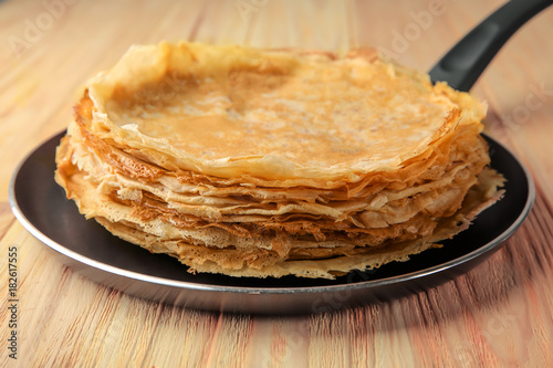 Pan with delicious thin pancakes on wooden table